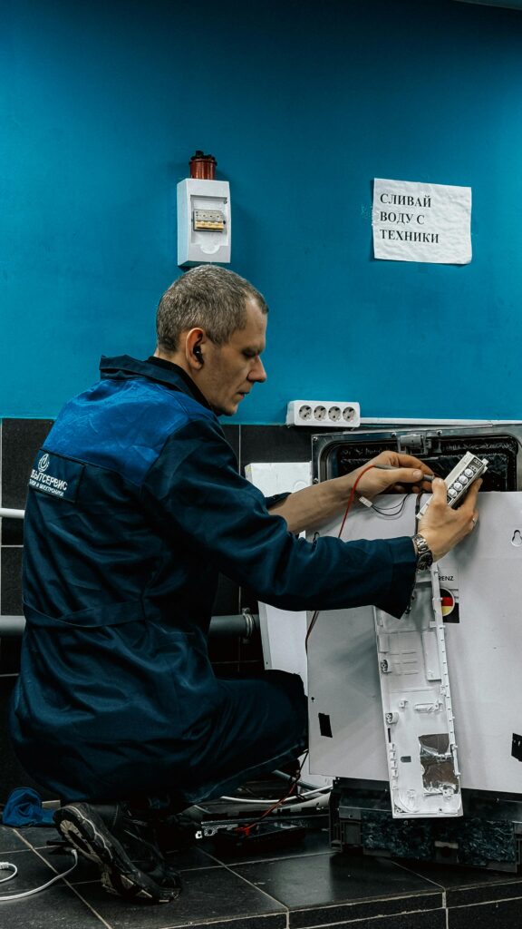 pexels-photo-34734504-34734504 A focused technician in blue uniform repairs a home appliance in an indoor setting.